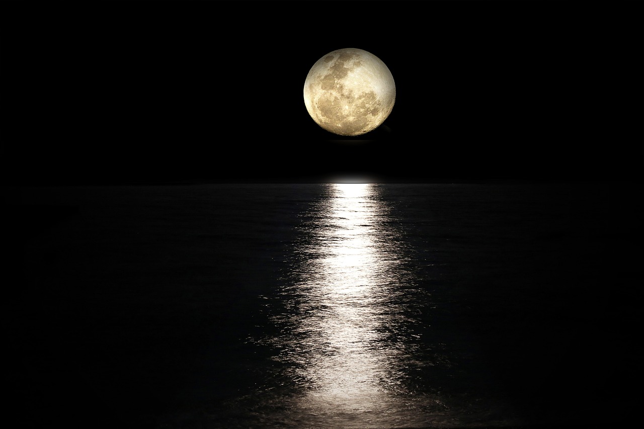 full moon over an ocean at night, the water reflecting its light