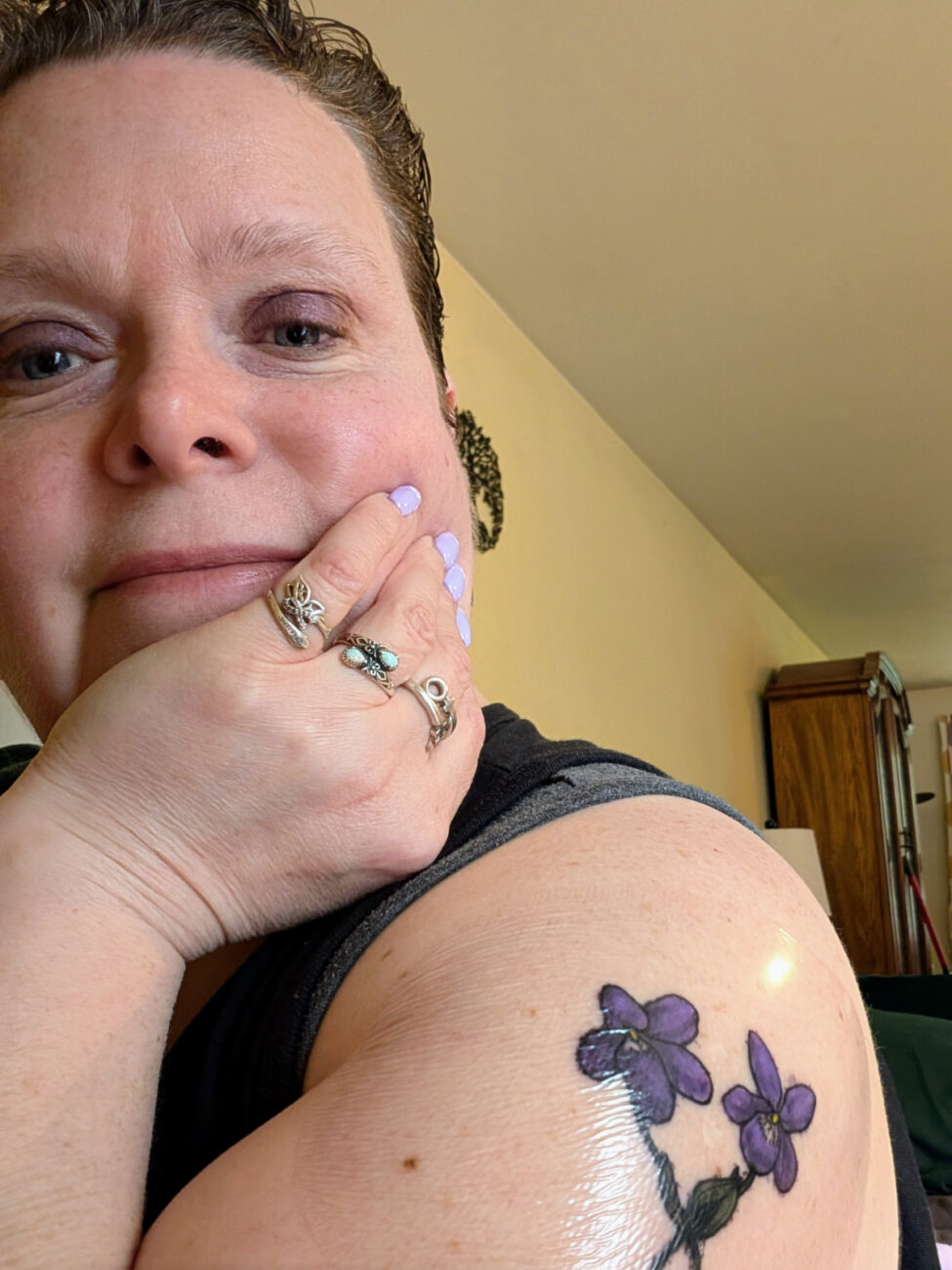 a selfie of me with my hand wrapped around my chin, smiling, showing off a brand new tattoo of a pair of violets overlapping at the stems