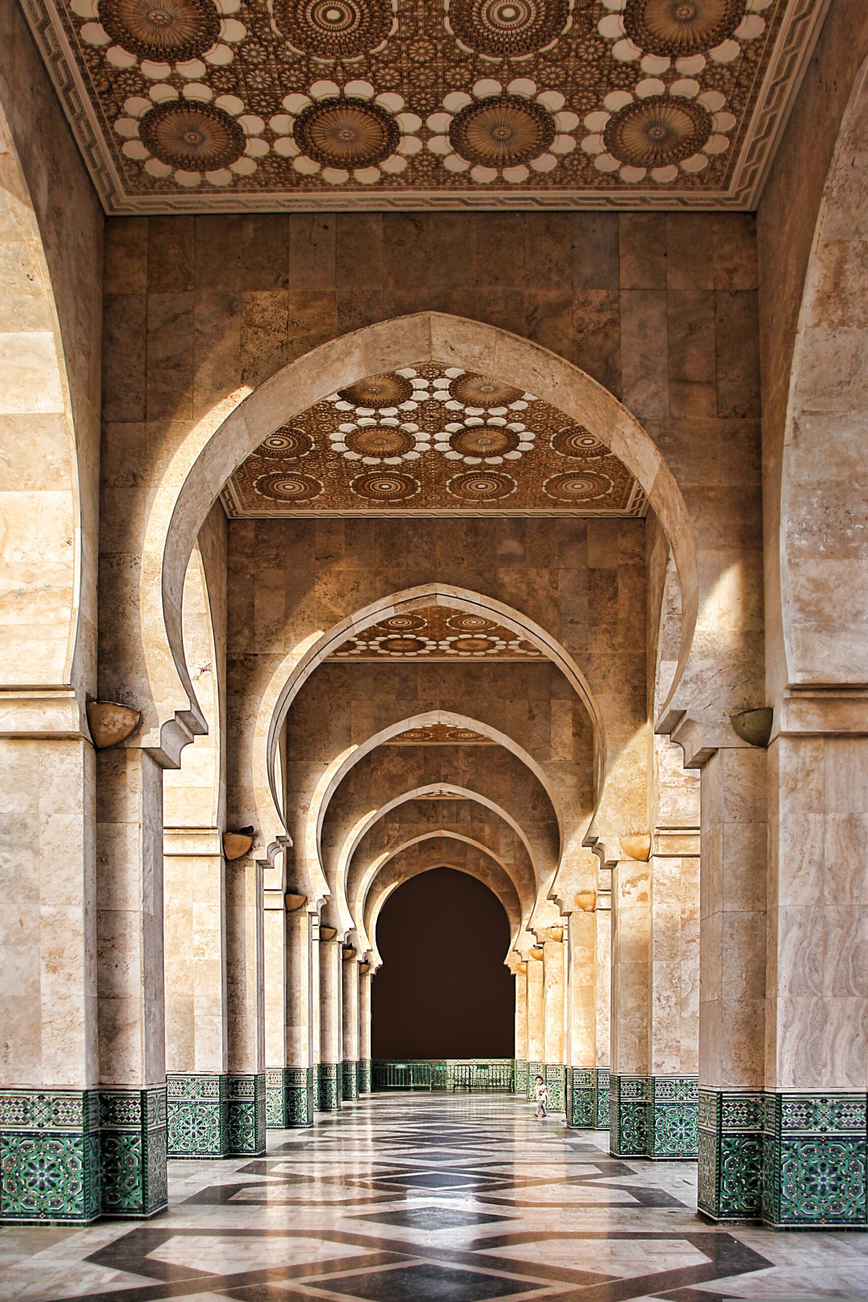 Image of a highly decorative Moroccan building, with a long keyhole-shape hallway with a blacked out center at its end