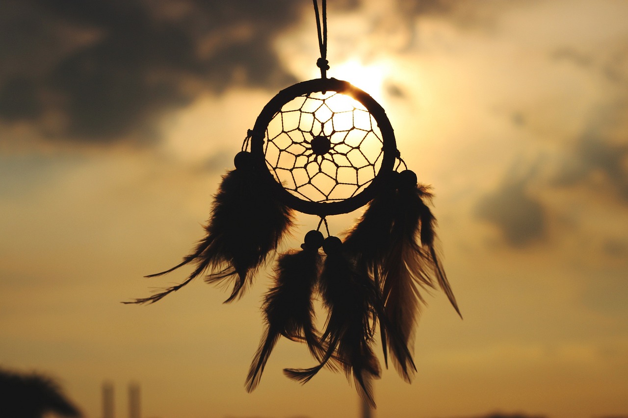 This image, used for the poem "I Dream, Nonetheless," is a picture of a dream-catcher held up in front of a sun obscured by clouds.