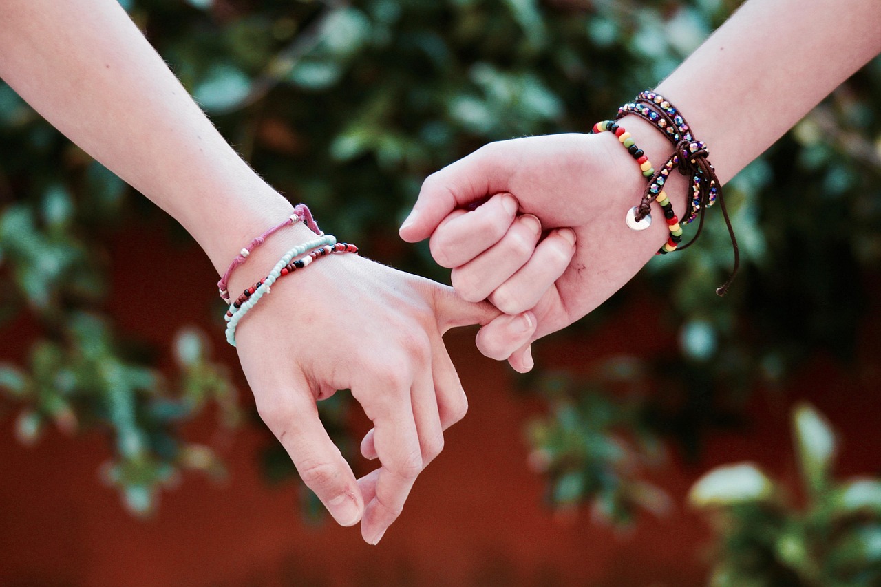 The story, "To Have And To Hold," is accompanied by an image of two women holding each other at their pinky fingers, wearing colorful bracelets on their arms. 